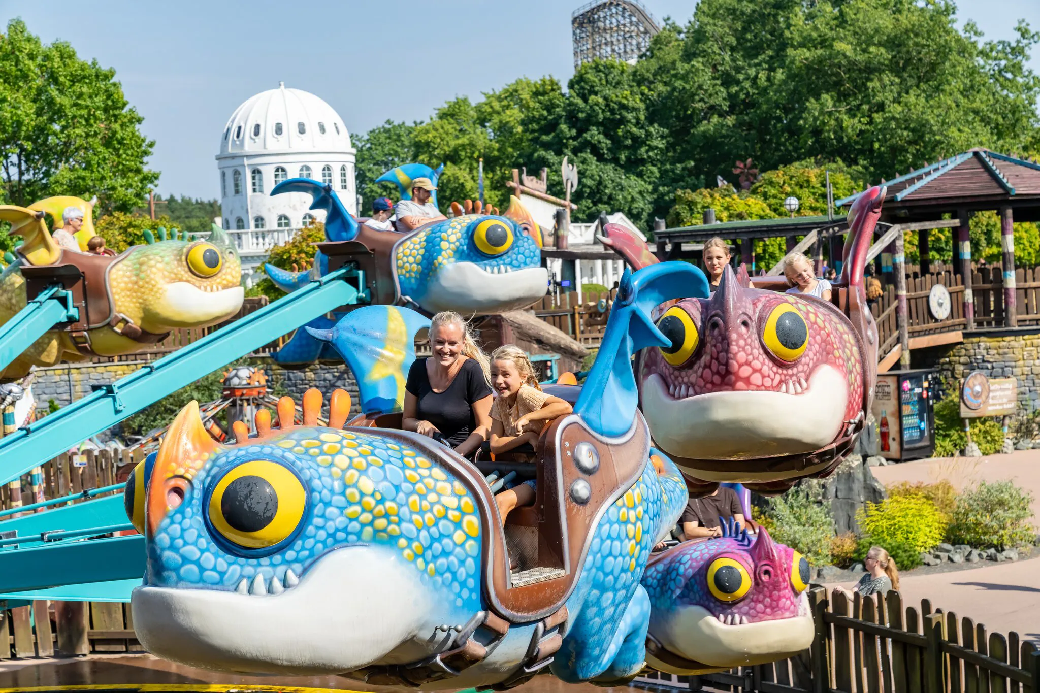 Kinder fahren fröhlich mit einem größen Drachen im Themenbereich „Drachenzähmen – Die Insel“ im Heide Park Resort.