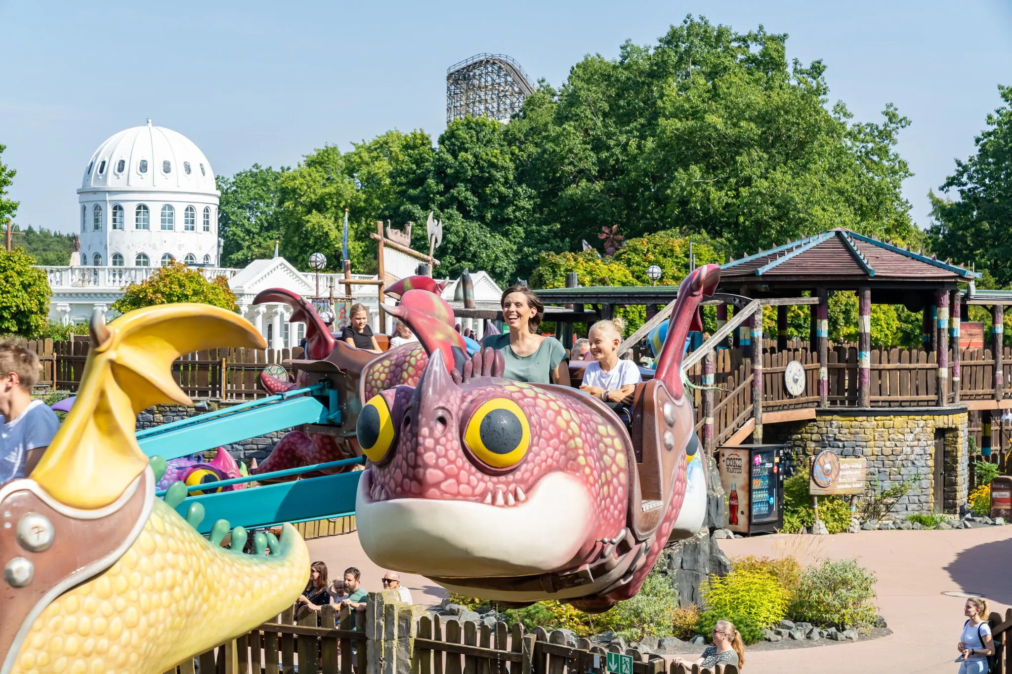 Kinder fahren in fliegenden Drachen über Wasser im Themenbereich „Drachenzähmen – Die Insel“ im Heide Park Resort.