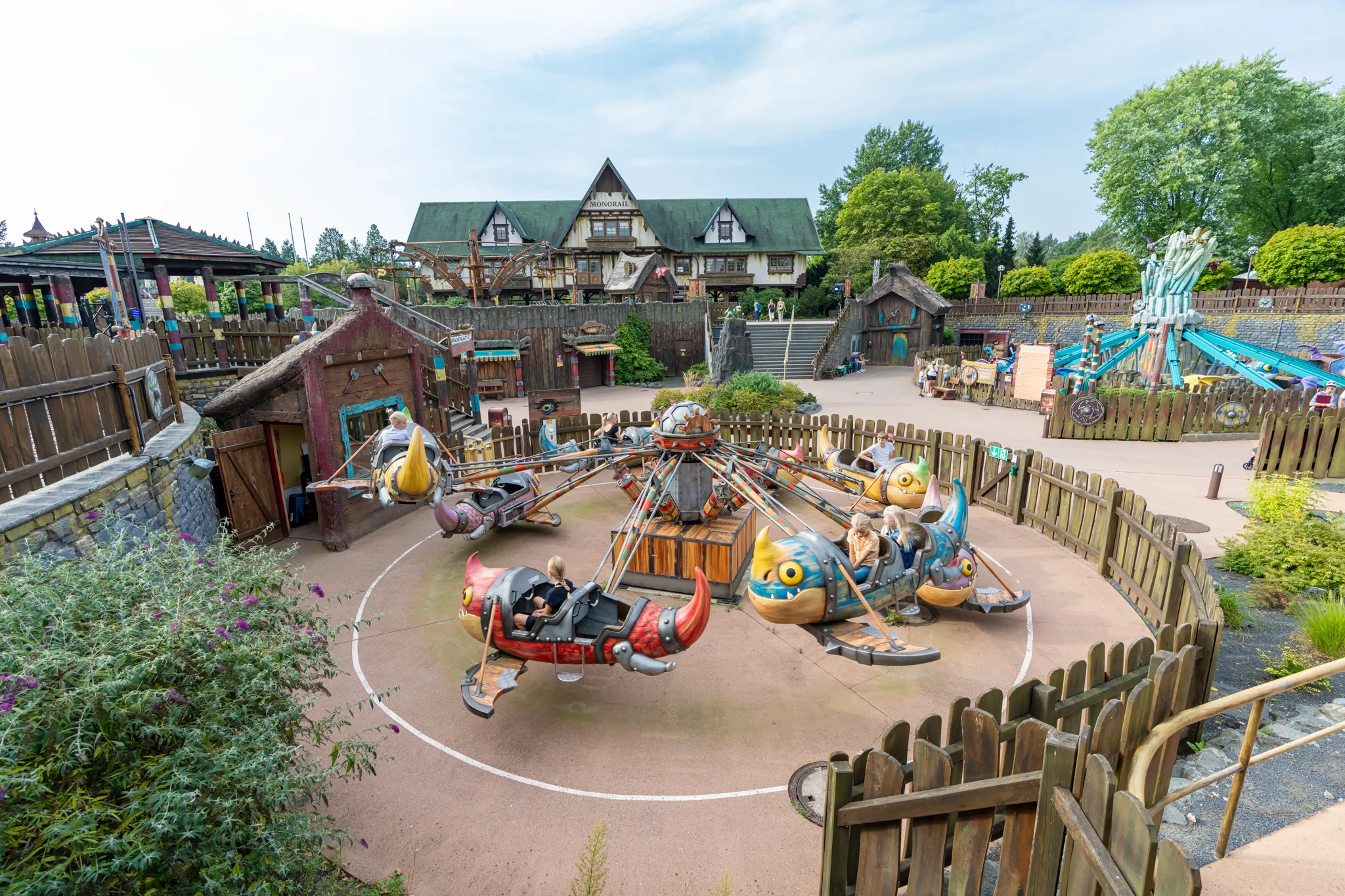 Besucher sitzen in den Gondeln von Grobians Wolkenspringer im Heide Park Resort. Die Gondeln sind bunte Drachen. Im Hintergrund sind weitere Drachenelemente.