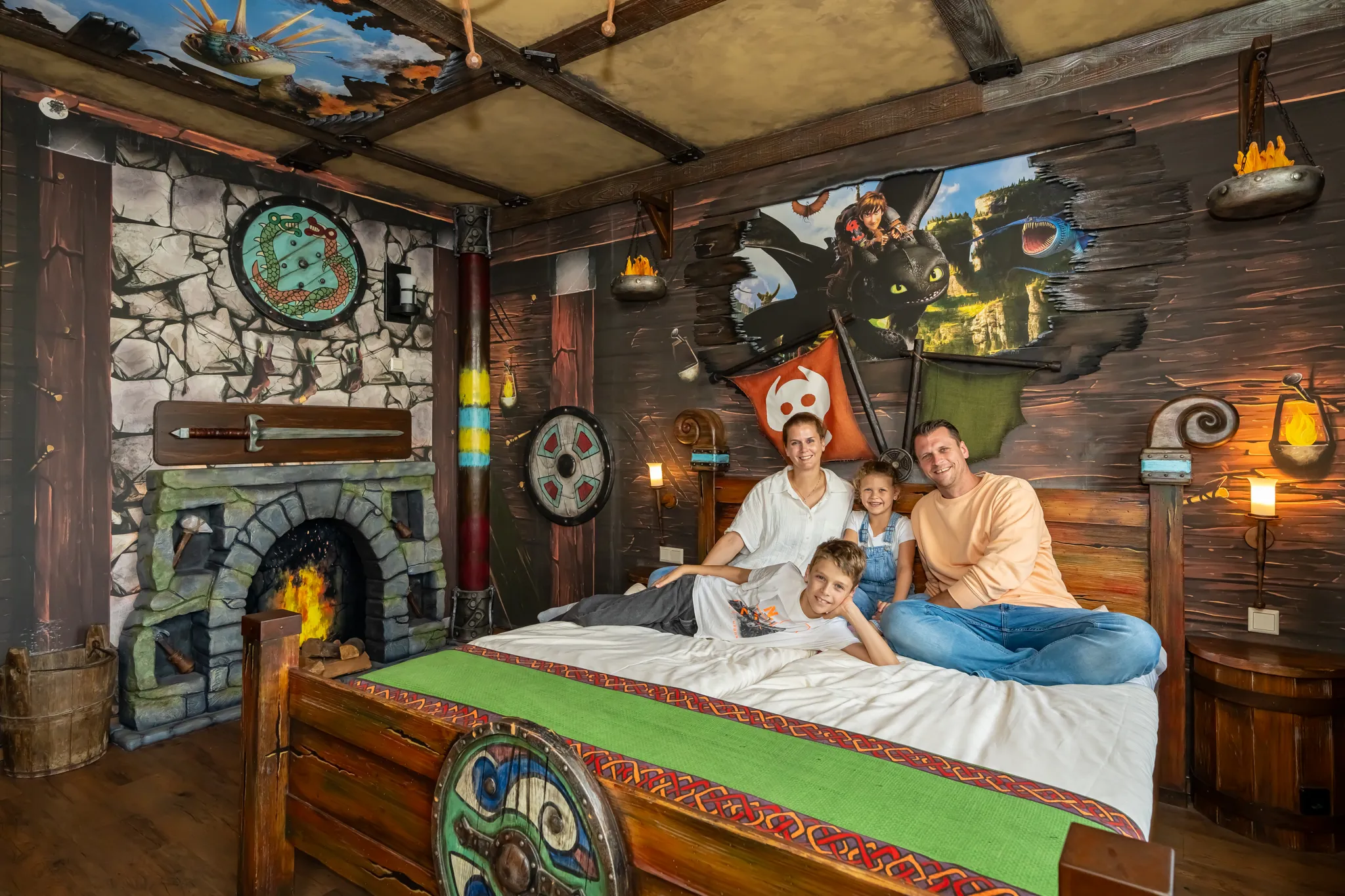 Eine vierköpfige Familie ist auf dem Bett im Drachenzimmer. Die Thematisierung ist von Drachenzähmen leicht gemacht mit Drachen- und Wikinger-Elementen.